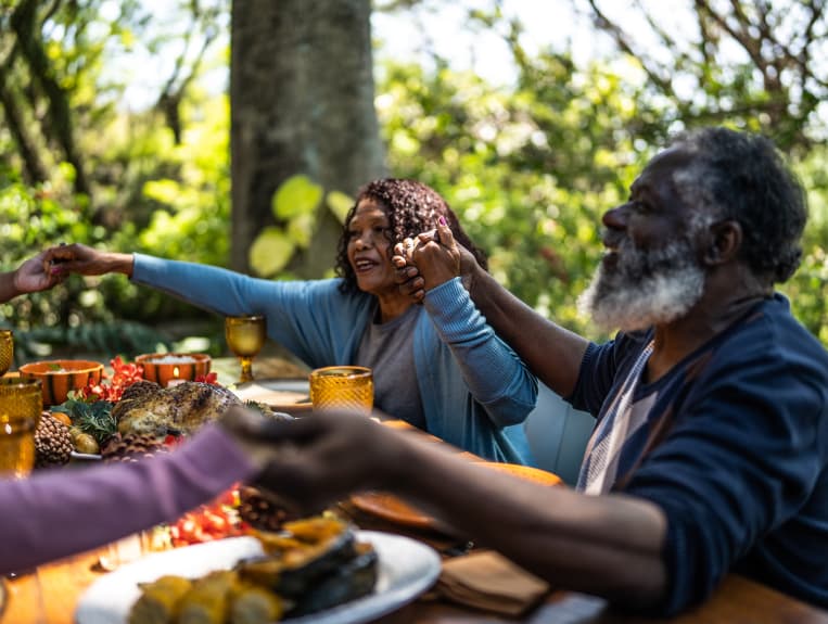 Family sitting around the dinner table with hands raised and clasped in a circle.